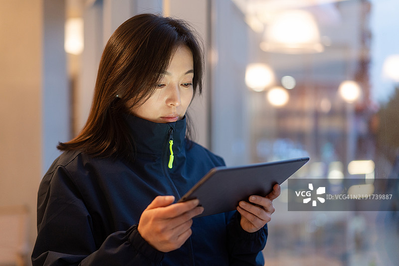 亚洲女性在办公室夜晚窗边使用数字平板电脑图片素材