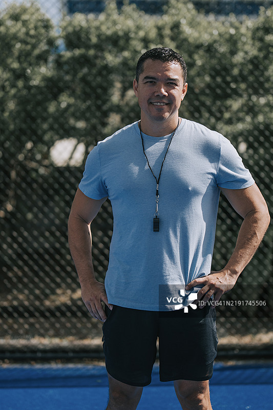 澳大利亚多种族男性教练微笑着看向镜头，站在运动场前。图片素材