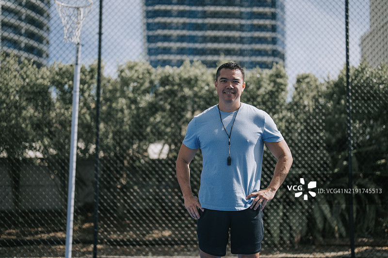 澳大利亚多种族男性教练微笑着看向镜头，站在运动场前。图片素材