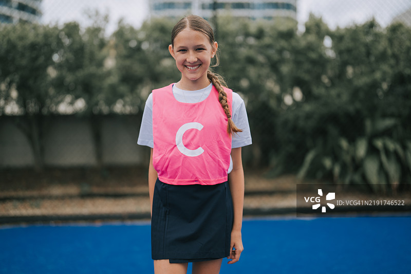 微笑着看向镜头的澳大利亚年轻女孩中场网球运动员，站在运动场上。图片素材