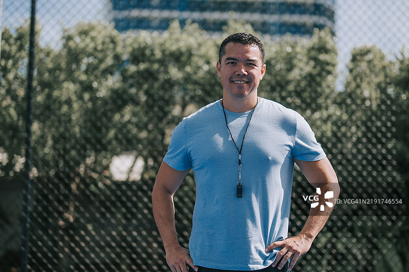 澳大利亚多种族男性教练微笑着看向镜头，站在运动场前。图片素材