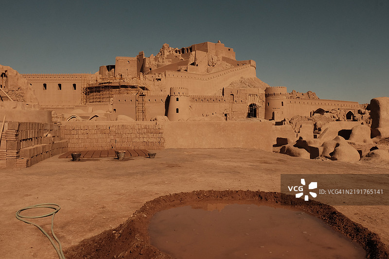 在伊朗克尔曼省的巴姆城堡前，阳光下的土坯砖正在地面上晾干，前方有一个泥坑，正在制作砖墙。图片素材