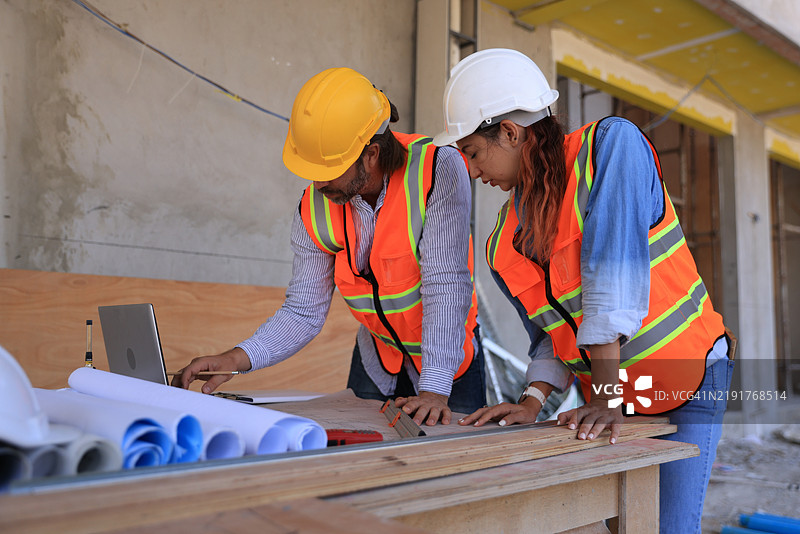 男性工程师和女性工头穿着安全背心在家居办公室施工现场一起查看蓝图图纸。图片素材
