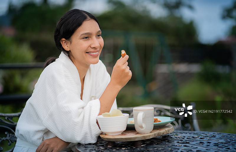 微笑的女性在户外穿着浴袍享受早餐图片素材