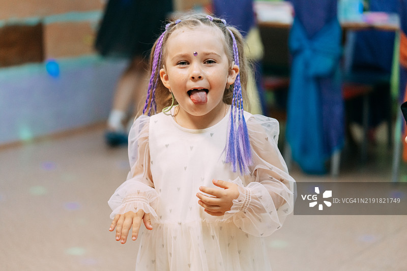 小女孩戴着人工耳蜗，吐着舌头，在生日派对上玩得很开心图片素材