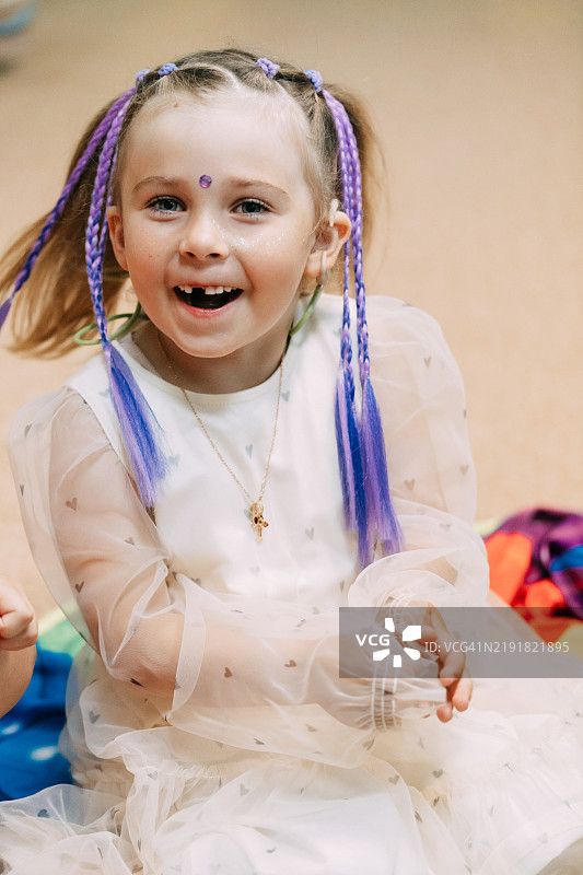 微笑的学龄前女孩肖像，佩戴耳蜗植入物，紫色辫子和白色裙子。图片素材