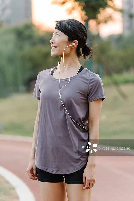 年轻的亚洲教练在户外热身时佩戴便携式耳机听音乐图片素材