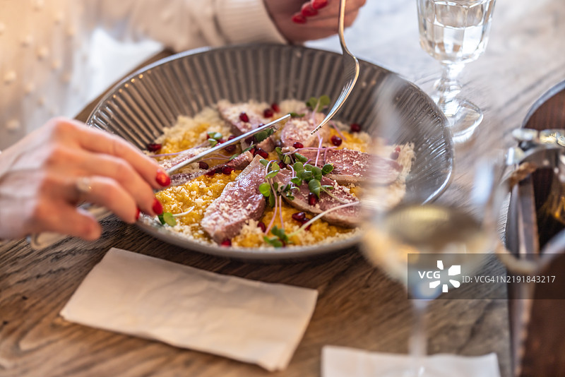 一位女性的手握着餐具，在餐厅里，她准备开始享用意大利烩饭配鸭胸肉。图片素材