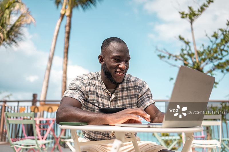 微笑的黑人男子在户外享受美食和笔记本电脑图片素材