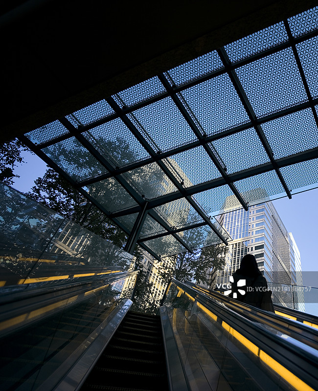 清晨，女性在自动扶梯上，抵达现代商业区。图片素材