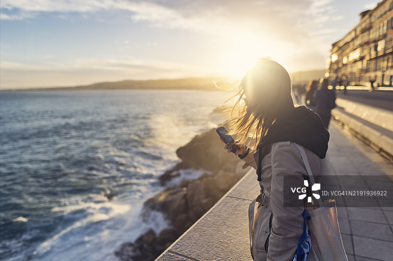 年轻女性在法国阿尔卑斯-海洋省尼斯市的海滨拍照。图片素材