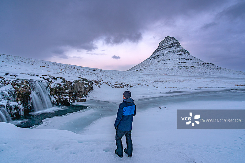 徒步旅行者欣赏冰岛斯奈法尔斯半岛上美丽的基尔基费尔山和基尔基费尔斯瀑布前色彩斑斓、戏剧性的日落图片素材