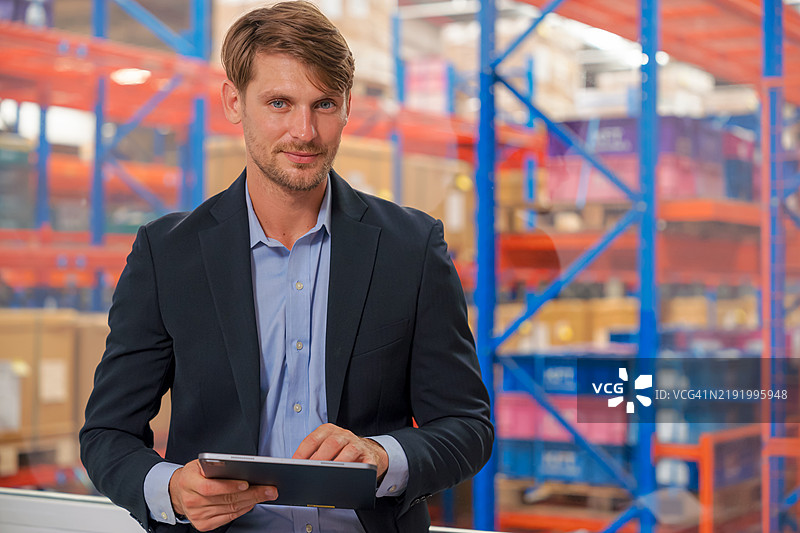 自信的男性仓库主管手持数字平板电脑，站在物流仓库内。图片素材