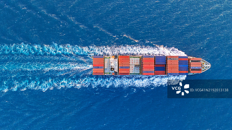 航拍视角下的集装箱船全速航行，海面上形成美丽的波浪图案，适用于物流。图片素材