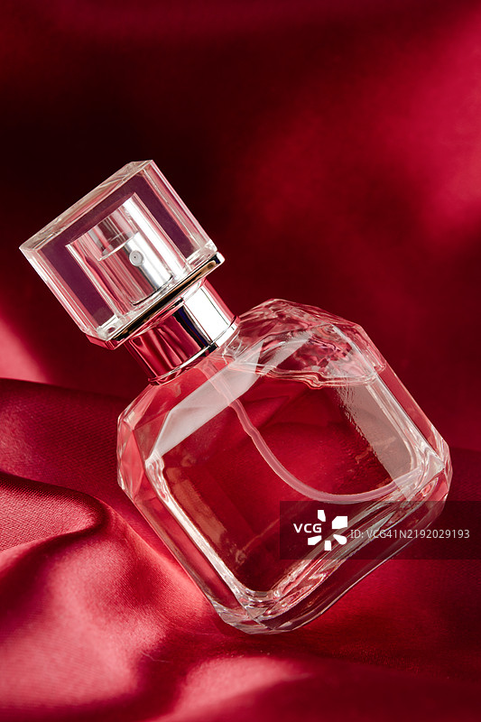 奢华香水瓶喷雾在红色缎面织物背景上。图片素材
