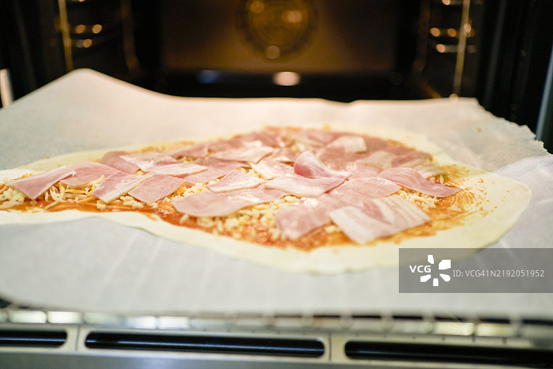 未烹饪的意大利香肠比萨饼放在家用烤箱中，准备烹饪，正面特写视图图片素材