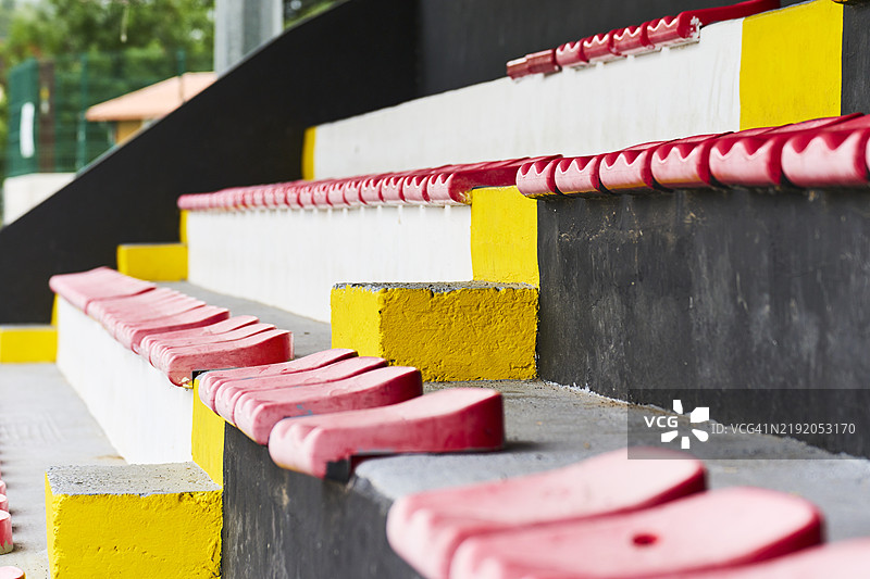 阳光明媚的日子里，空旷的场地上排成一排的红色看台侧面视图。图片素材