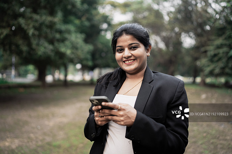 美丽的中年女性在商务中心外走路并用手机发短信图片素材