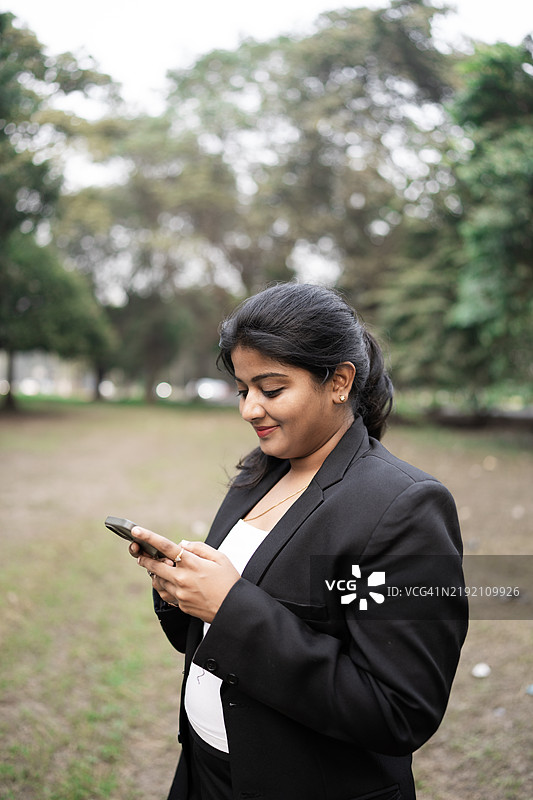 美丽的中年女性在商务中心外走路并用手机发短信图片素材
