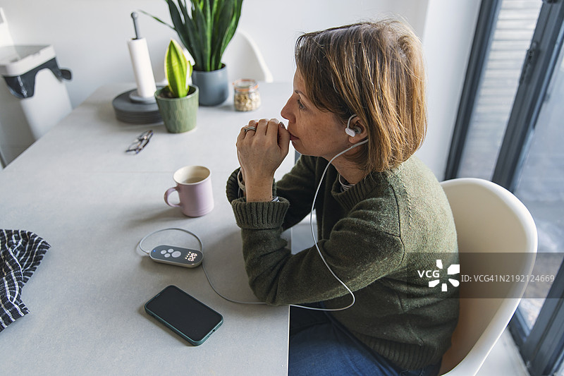 一位成熟的女性在餐桌旁使用迷走神经刺激（神经调节）医疗设备。图片素材