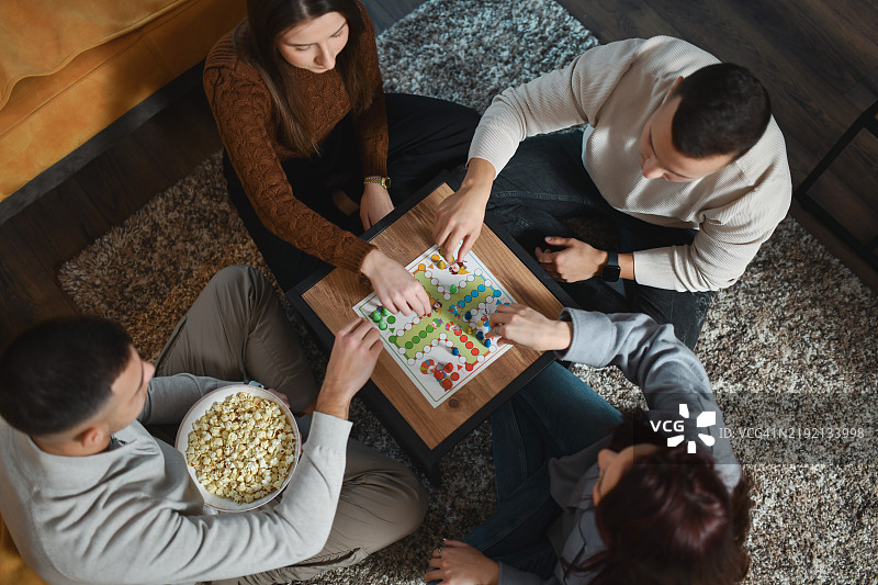 一群男女朋友在家里度过星期六晚上，玩飞行棋，吃爆米花。图片素材