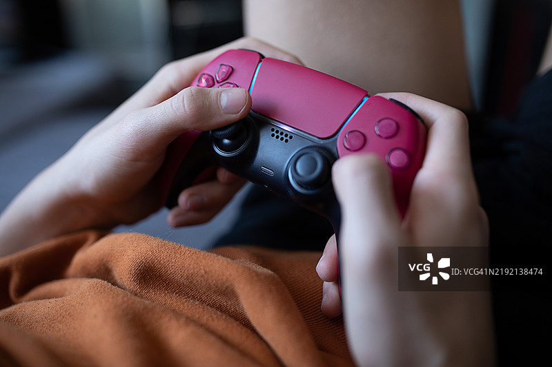 特写镜头，手握着一款色彩鲜艳的双色游戏手柄。此人正沉浸于游戏中，手柄成为画面的中心焦点。场景传达出休闲和家庭娱乐的氛围。图片素材