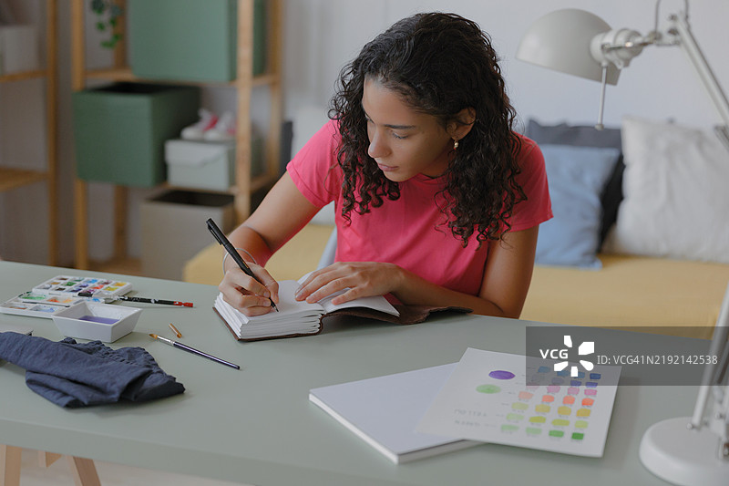 年轻艺术家在家中的工作室里绘制素描并在笔记本上做笔记图片素材