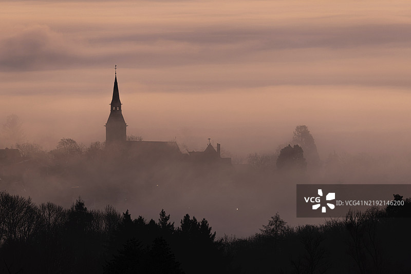 晨曦前，薄雾飘荡在克龙贝格镇（Kronberg im Taunus）中，只有圣彼得和圣保罗教堂的尖塔显得格外突出。克龙贝格，马勒布里克，黑森州，德国，欧洲图片素材