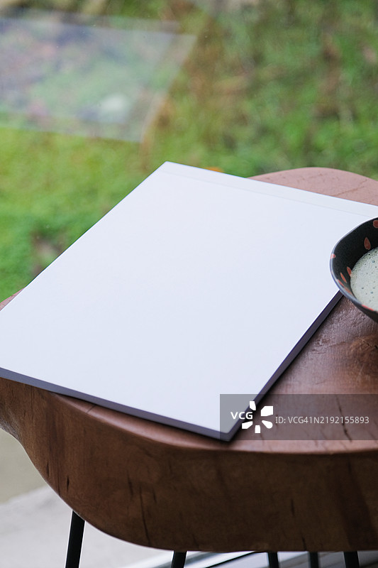 咖啡桌上的空白杂志样本，旁边有绿茶抹茶，窗边光线明亮。图片素材