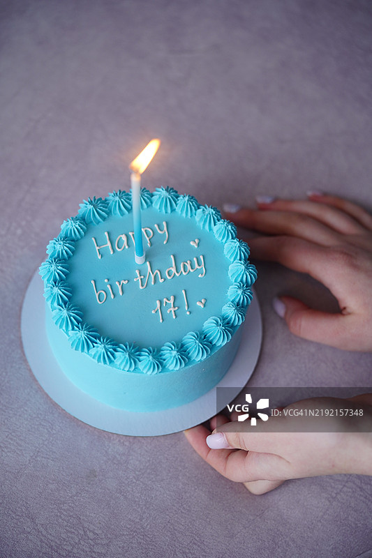 两只手捧着一个小巧的点燃的生日蛋糕，上面有蓝色的糖霜图片素材