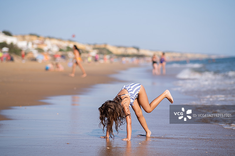 穿着比基尼的女孩在海滩的岸边做杂技图片素材