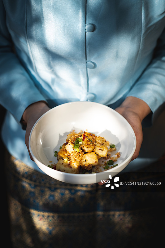 白碗盛着腰果鸡，旁边是一位身穿传统泰国服饰的人士图片素材