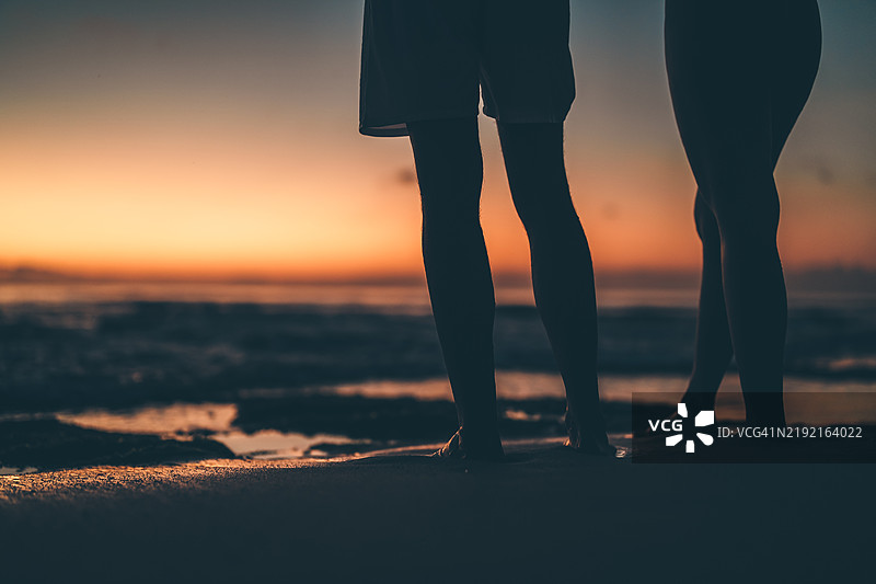 一对情侣在海滩上并肩而立，背景是绚丽的海洋日落。图片素材