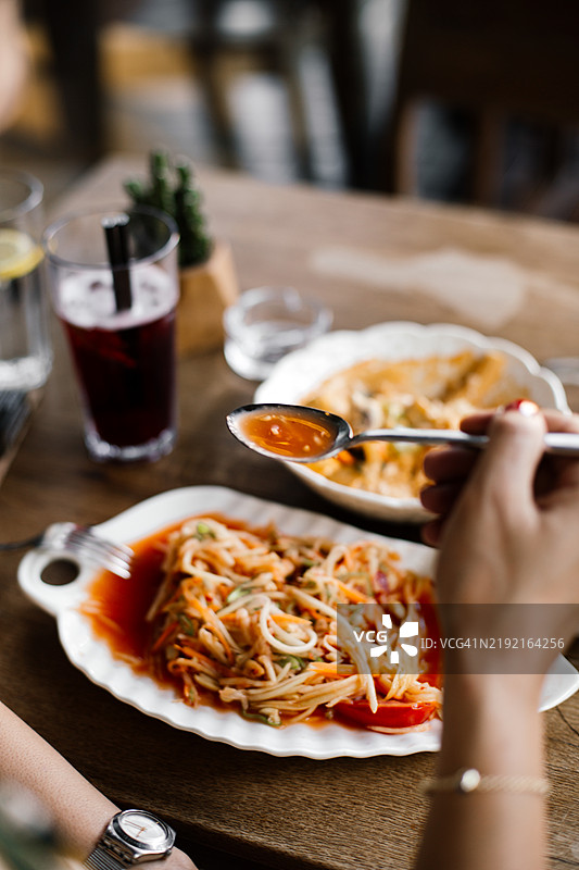 传统泰式青木瓜沙拉，辛辣酸爽的青木瓜沙拉，配有新鲜香草、辣椒和青柠汁，正宗泰国街头美食，盛放在温馨的餐桌上白色盘子里图片素材