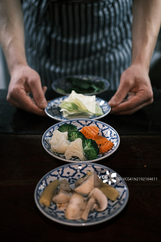 一位厨师在泰国餐厅为泰国菜准备新鲜蔬菜，展示整齐摆放的蘑菇、卷心菜、西兰花和胡萝卜，捕捉传统泰国烹饪中新鲜食材的精髓。图片素材