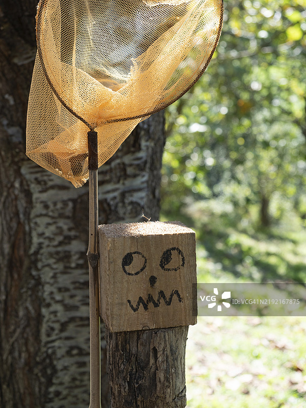 木桶上画着一张搞笑的面孔，眼睛斜视，嘴巴扭曲，旁边有一个捕蝴蝶的人。被困的概念。图片素材