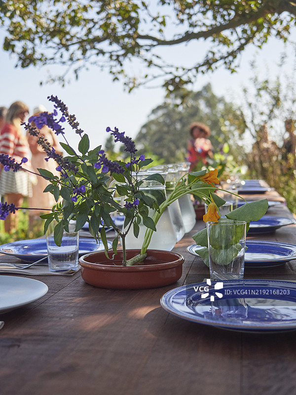 阳光明媚的夏日假期庆祝活动中，紫色花朵摆放在木桌上，周围有餐具和玻璃杯。图片素材