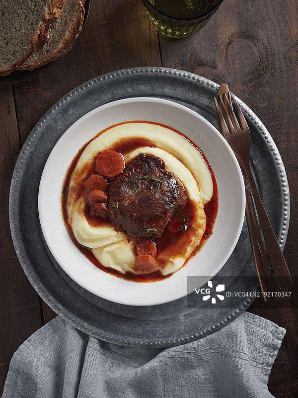 炖猪脸颊肉配胡萝卜和肉汁，搭配土豆泥。西班牙菜。俯视图，盘子放在木桌上。图片素材