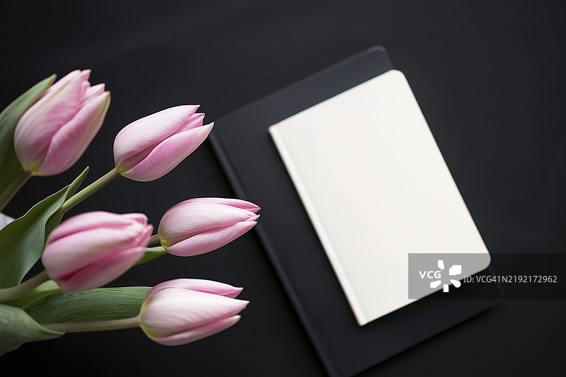 粉色郁金香和一本白色笔记本在黑色背景上图片素材