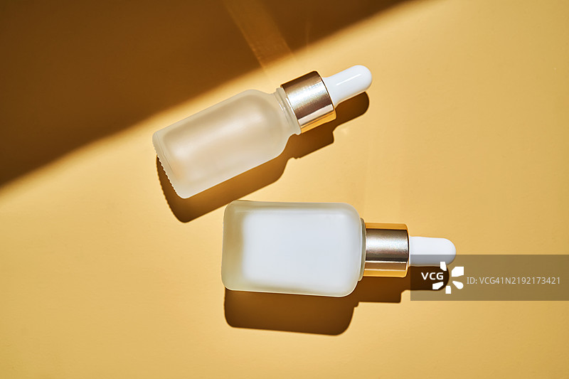 两瓶精华液在米色背景上，投射出美丽的阴影。图片素材