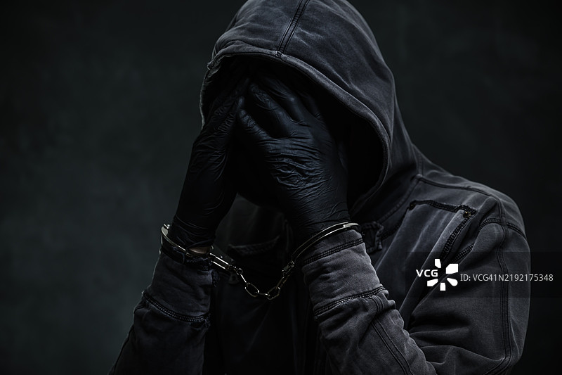 戴着连帽衫、用手遮住脸的手铐犯人图片素材