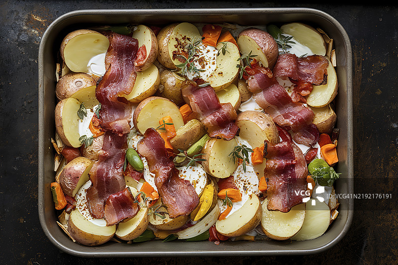 烤箱中烤制的切片土豆和培根，配有酸奶油和蔬菜图片素材