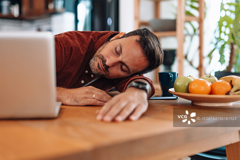 疲惫的商人在桌子上睡着，手边是笔记本电脑。图片素材