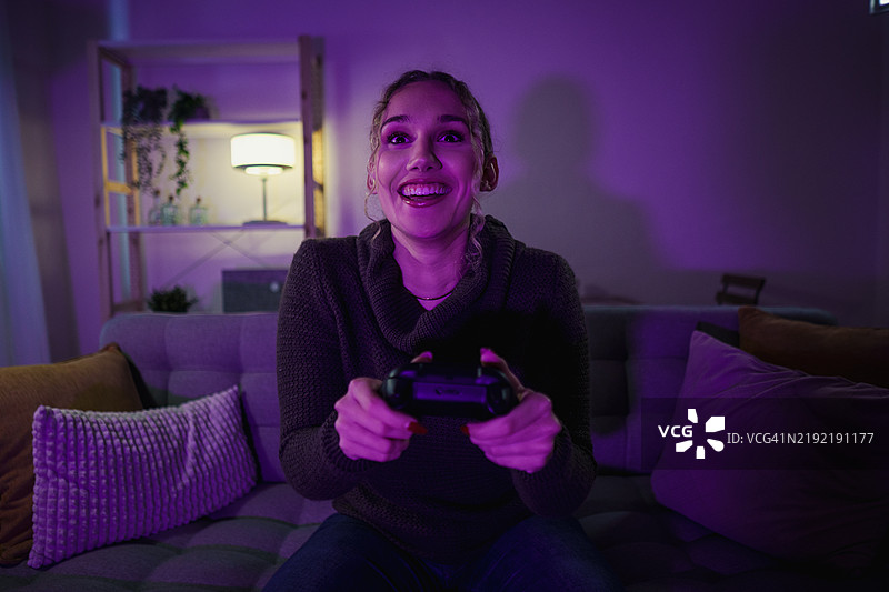 兴奋的年轻女性在家里的沙发上夜晚玩电子游戏图片素材