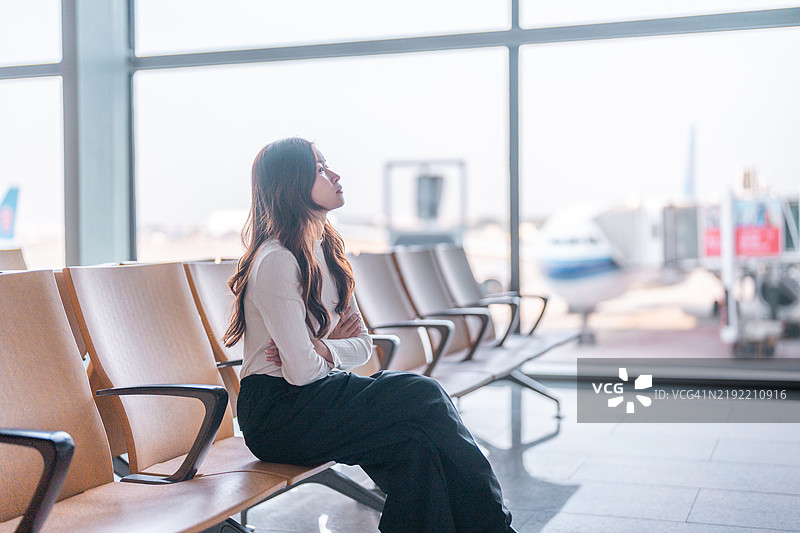 一位年轻的亚洲女性正在机场使用智能手机查看到达和出发信息板及航班时刻表。图片素材