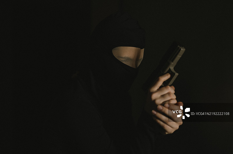黑色背景下的女性持枪盗贼。图片素材