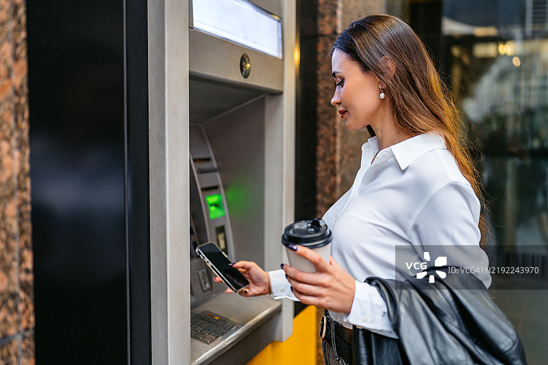 年轻女性在澳大利亚悉尼的ATM机上使用手机取款图片素材