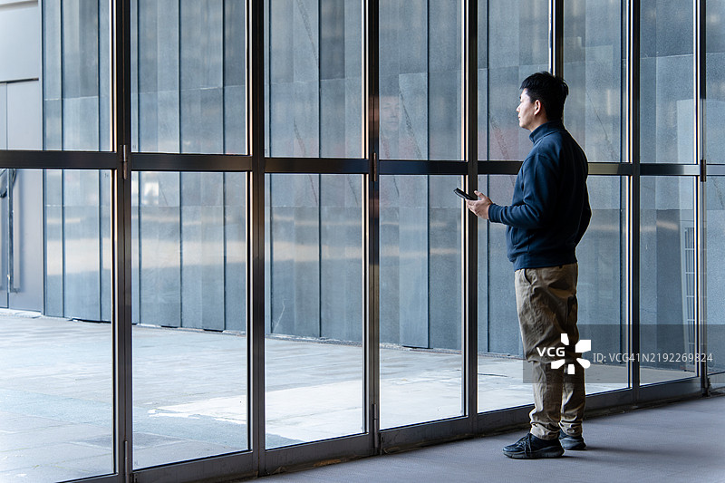 亚洲商人手持智能手机站在窗边图片素材