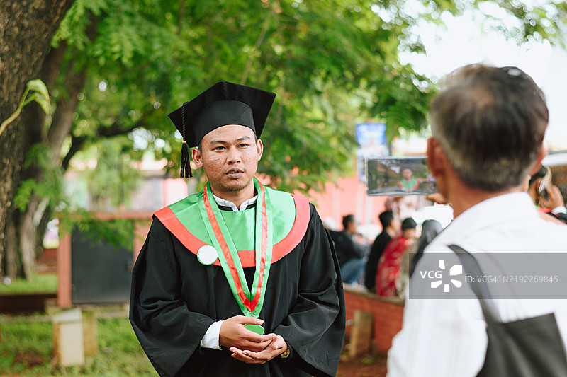 年轻男子穿着毕业袍接受一位陌生人的采访图片素材