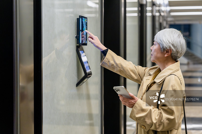 亚洲高级女商人使用面部识别技术打开办公大楼的门。图片素材